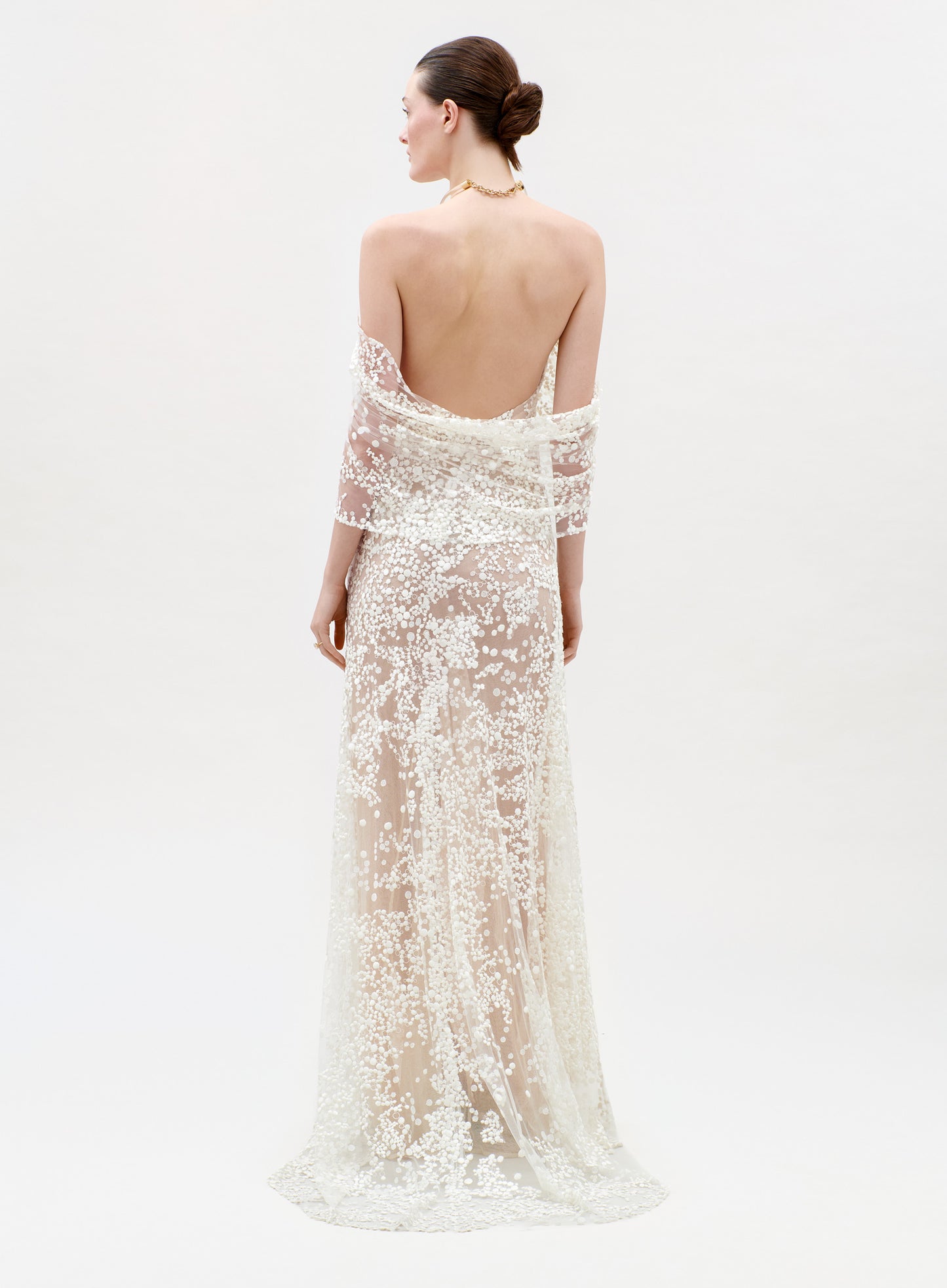 Woman wearing a white lace evening gown with a sheer overlay on a light gray background
