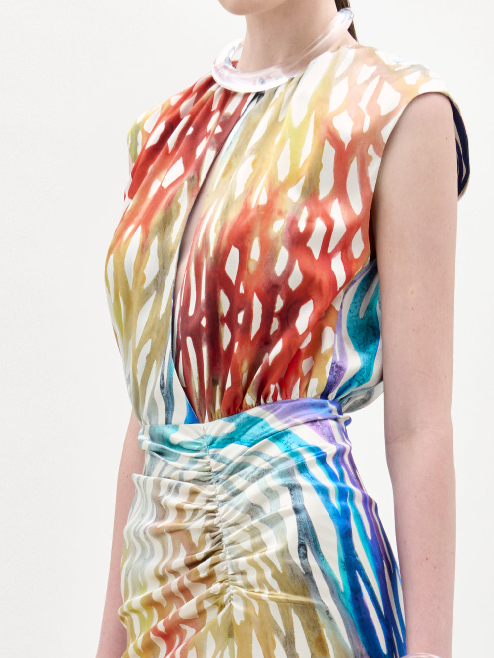 A woman stands against a plain background wearing the Samaira Dress, a sleeveless maxi with a ruched waist and a vibrant red, blue, yellow, and white abstract pattern.