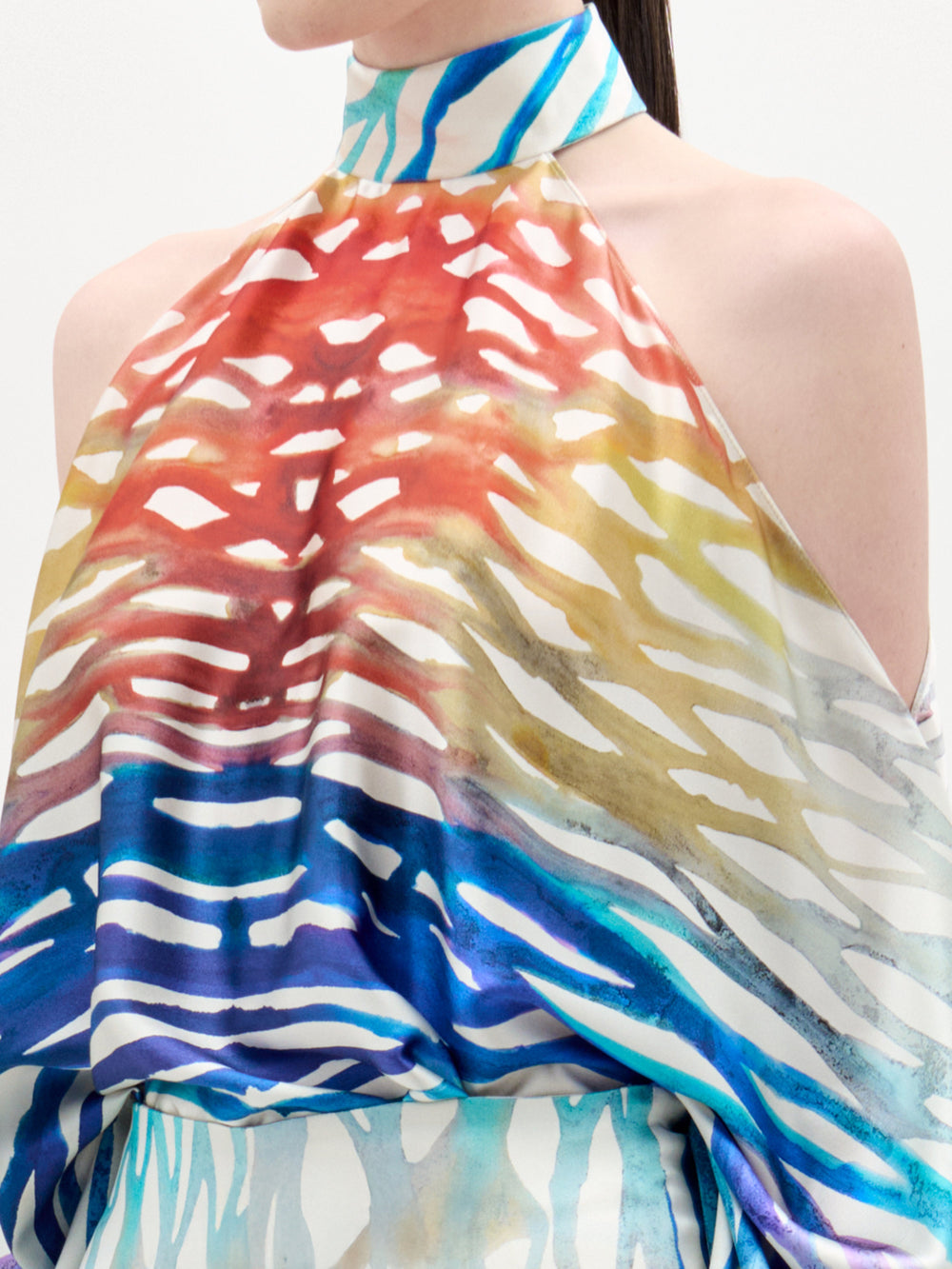 A woman models the Safira Blouse—an off-shoulder top featuring a colorful, abstract print in luxe Italian fabric—paired with matching wide-leg pants, set against a plain white background.