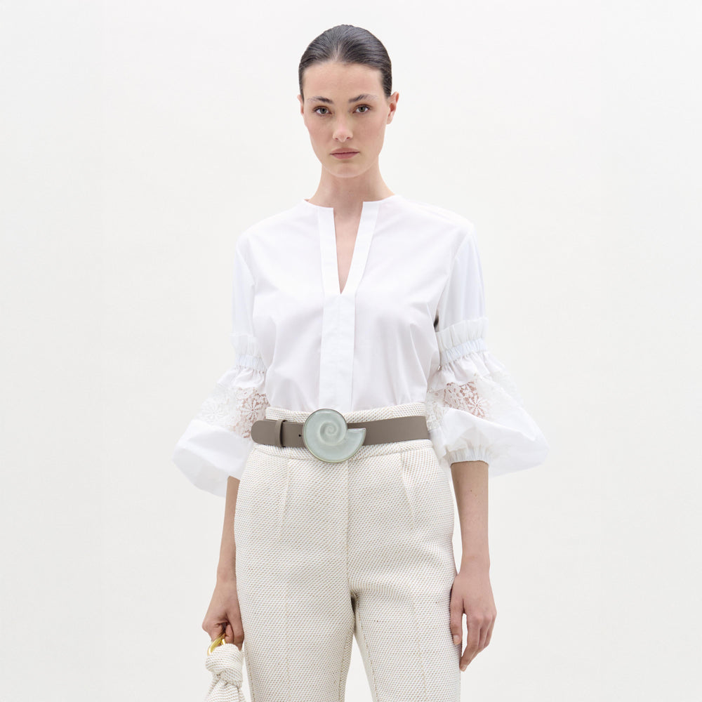Woman wearing a white blouse and beige pants with a belt on a white background