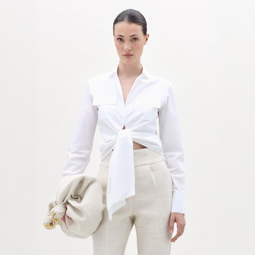 Woman wearing a white tied blouse and beige pants on a white background
