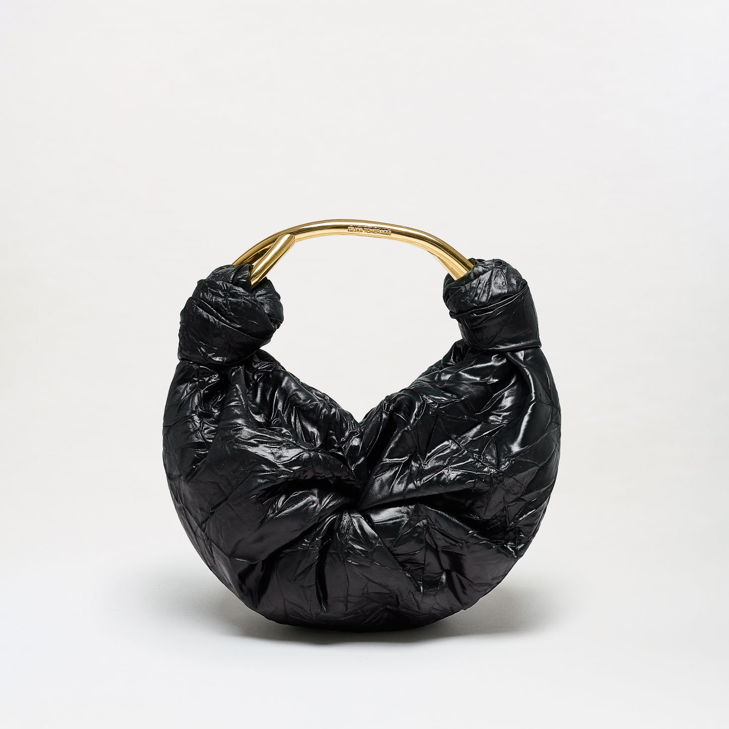 The Sofia Bag (Small) is a black, crescent-shaped bag crafted from luxurious Italian fabric, featuring a crinkled texture and finished with a shiny gold-toned curved handle. It is presented against a plain light background.