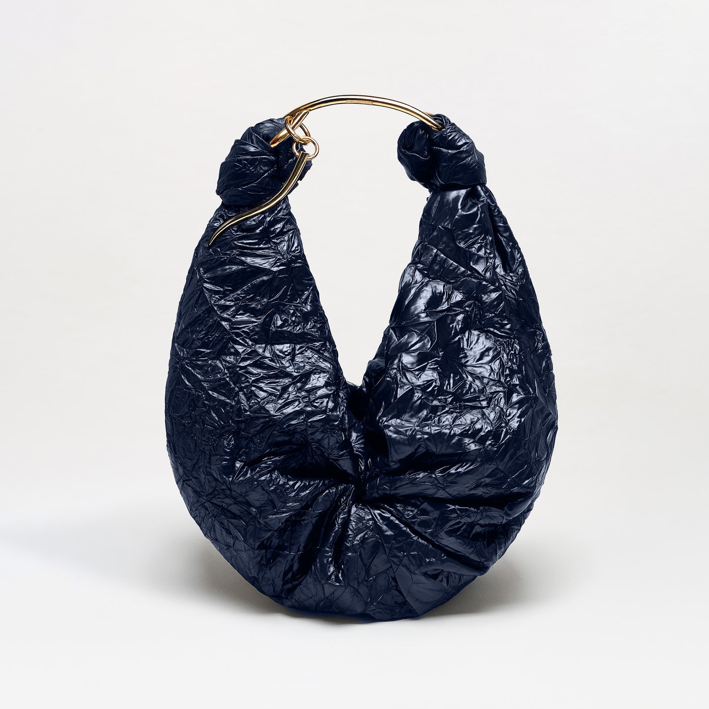 The Sofia Bag (Maxi) is a large navy blue crescent-shaped handbag with a crinkled texture and a bold gold-toned handle, crafted from Italian fabric, shown against a plain white background.