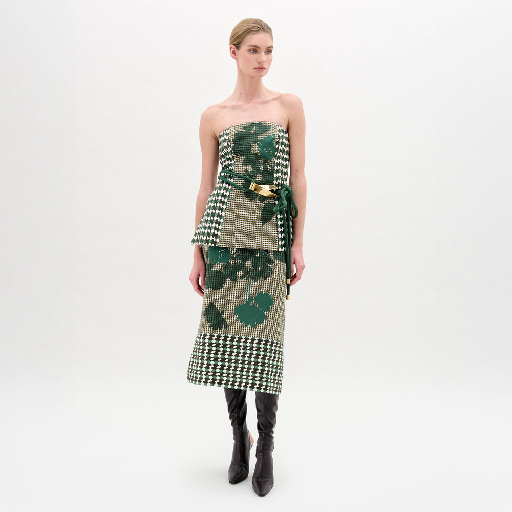 Woman wearing a green patterned top and green skirt with black knee-high boots on a white background
