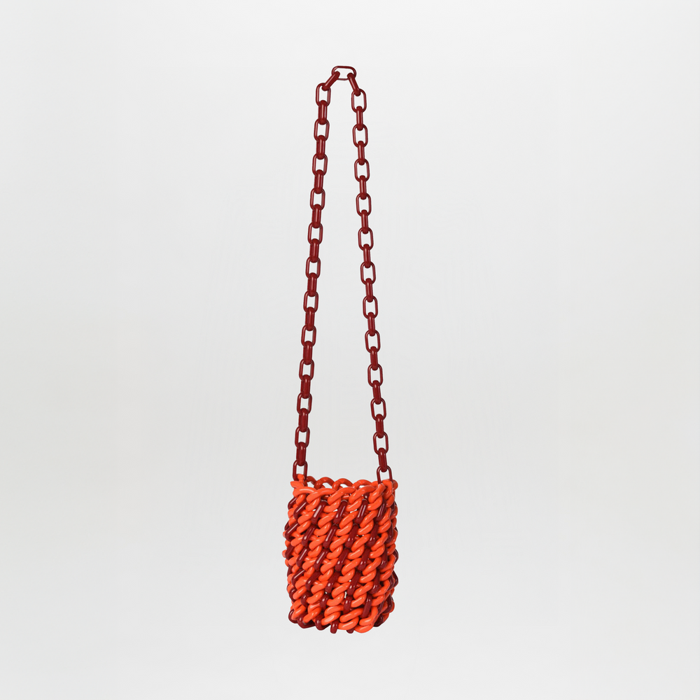 The Anise Bag Red is a small rectangular handbag with an orange resin body, chunky twisted design, and a long red chain strap, displayed against a plain white background.