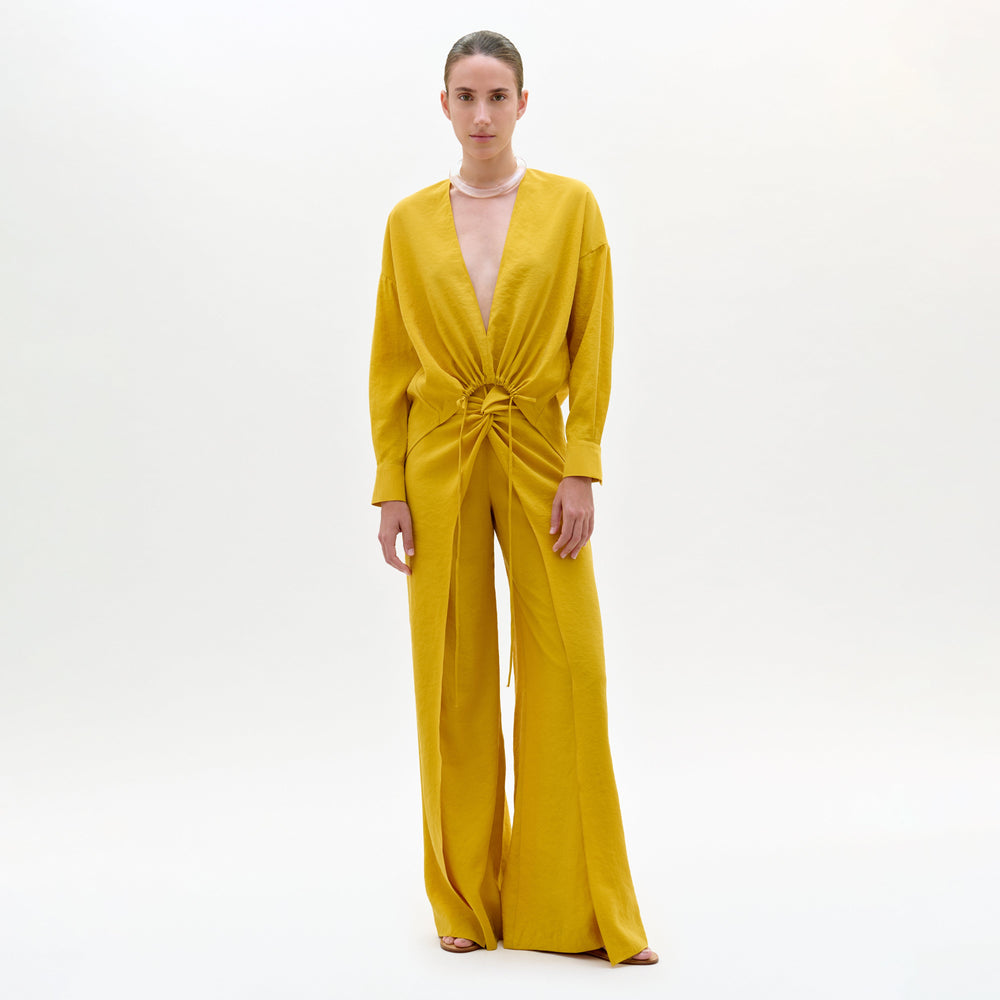 Woman wearing a mustard yellow jumpsuit on a white background
