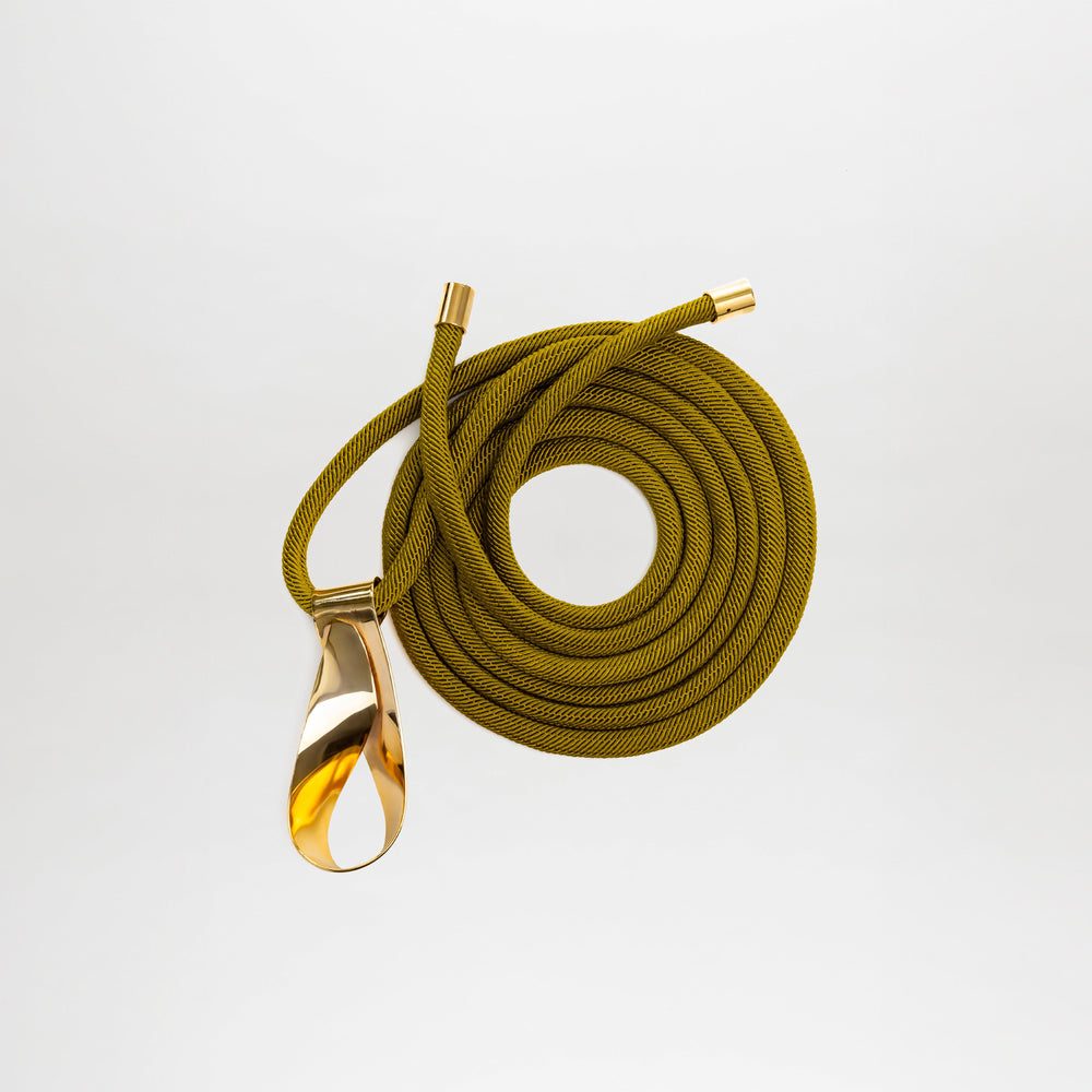 The Daiana Belt is a coiled olive green Italian cord belt with gold metal ends and a teardrop-shaped gold-plated brass buckle.