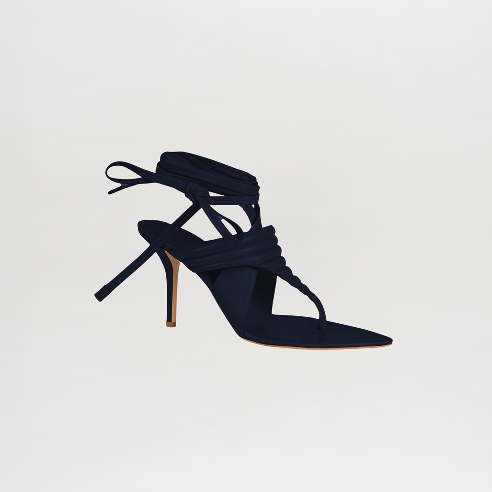 The Dalila Heels Navy is a single high-heeled sandal in Italian calf leather, featuring a strappy design, ankle wrap ties, and a thin stiletto heel, displayed against a plain white background.