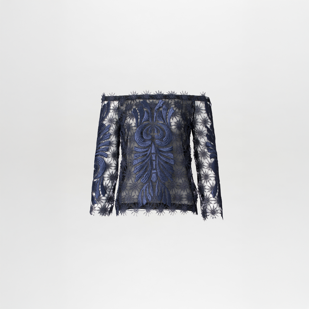 On August 19th, a person with slicked-back hair wears the Lala Blouse Navy with intricate patterns and high-waisted navy pants against a plain blue background.