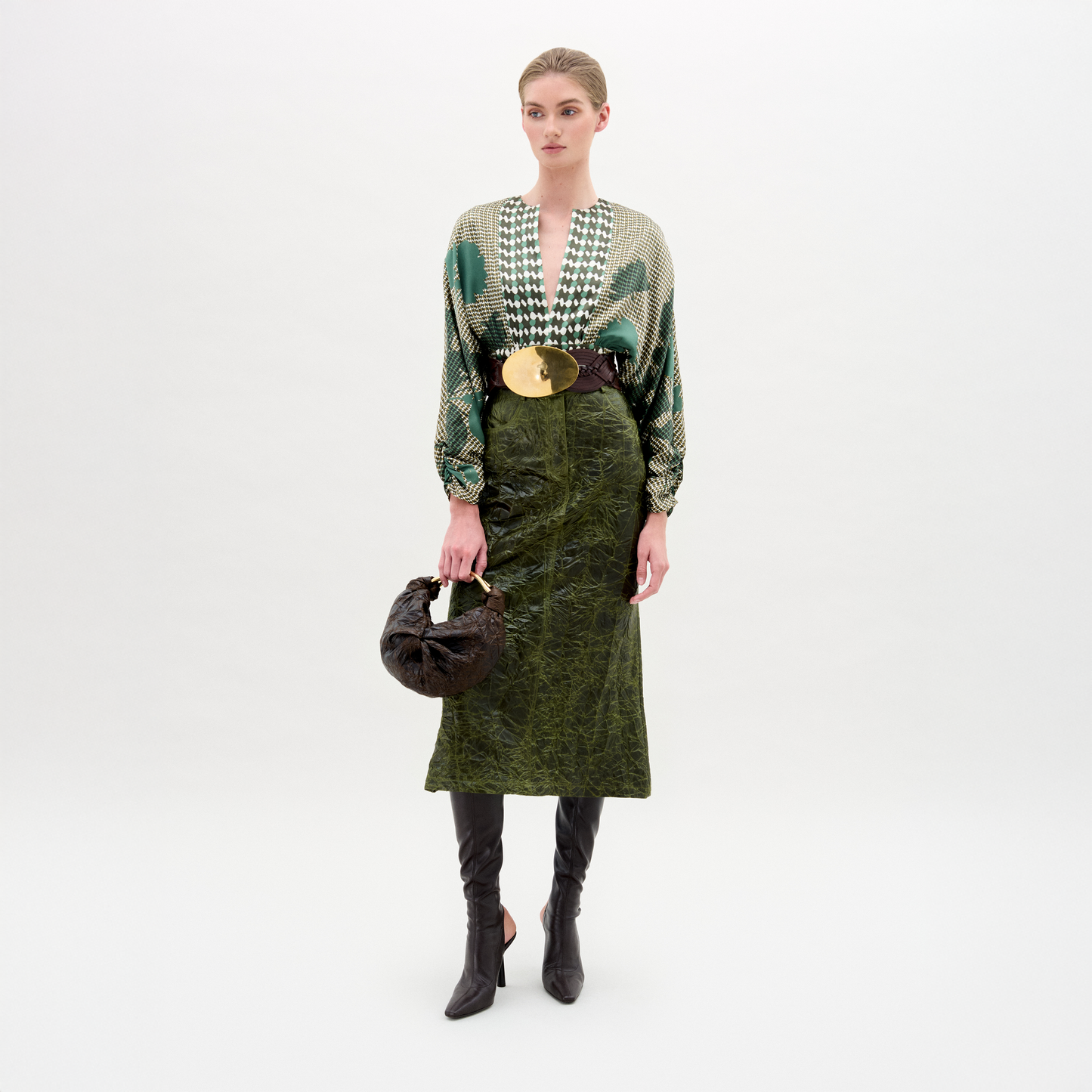 Woman wearing a green patterned top and green skirt with black knee-high boots on a white background