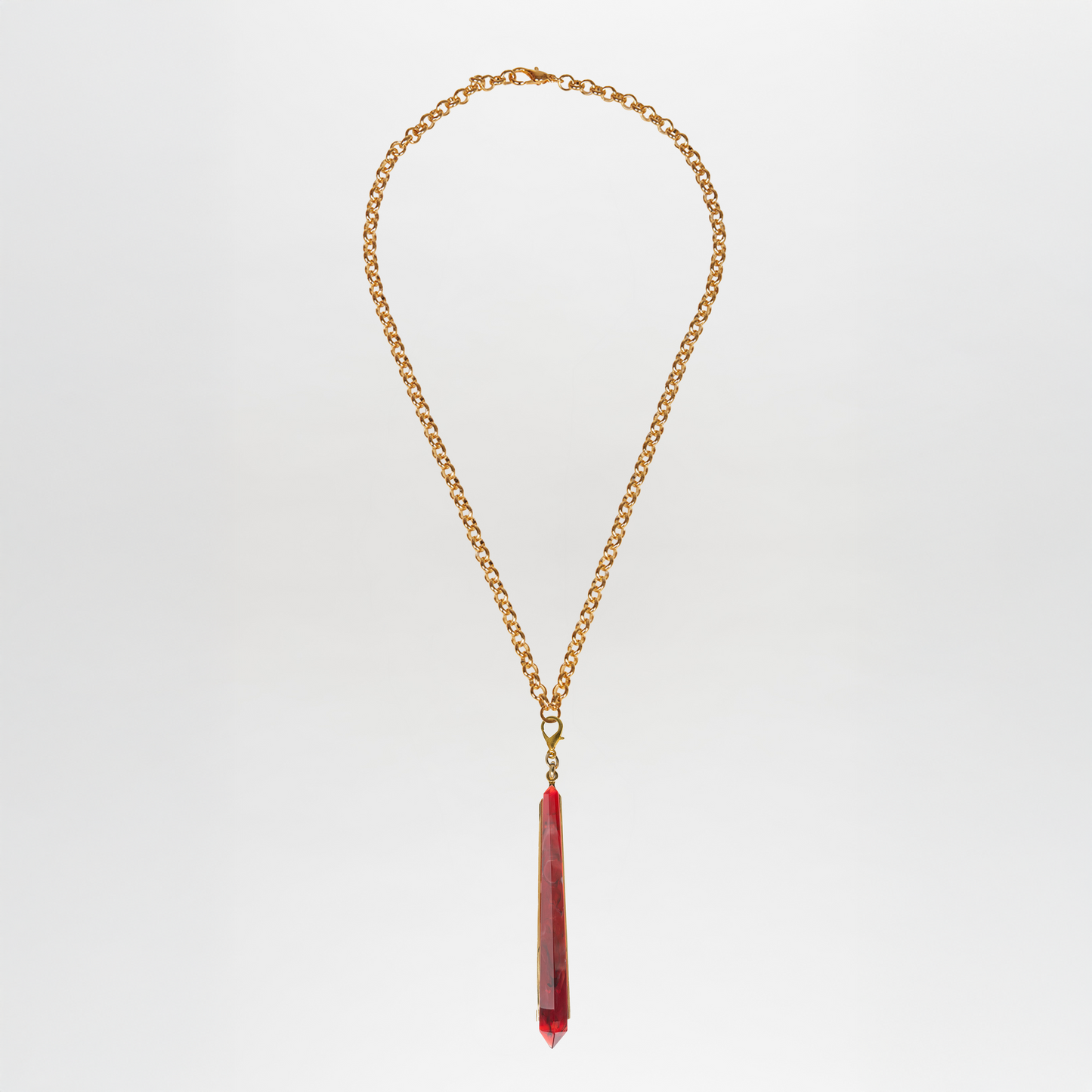 The Montse Necklace features a gold chain with a long, faceted Petralux® stone geometric pendant at the center, displayed against a plain white background.