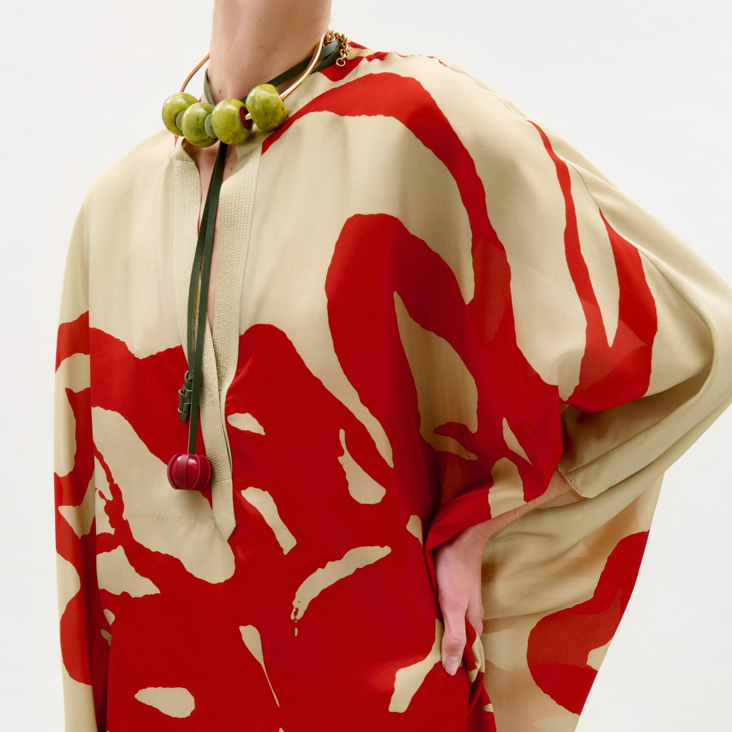 Person wearing a red and beige patterned garment with a necklace.