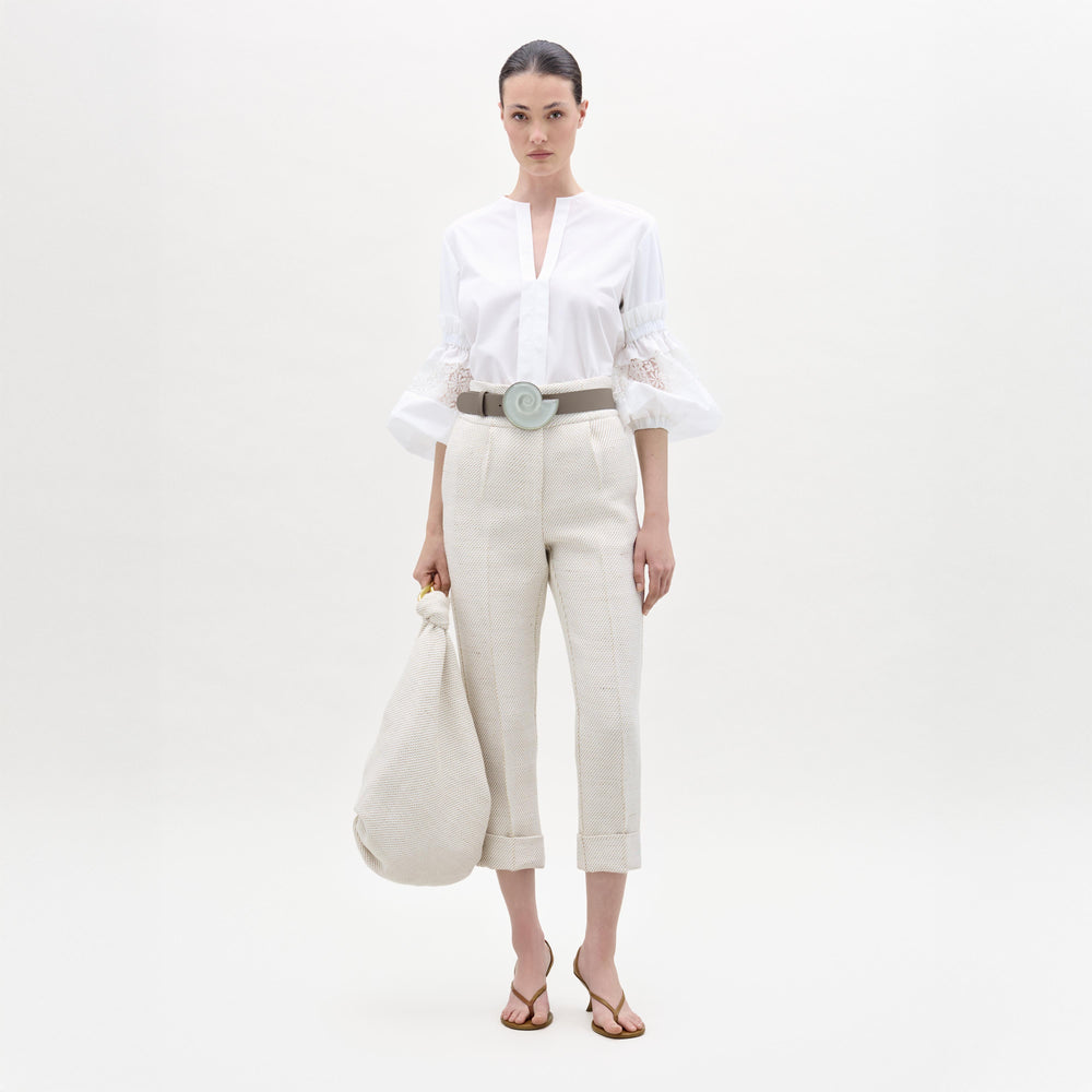 Woman wearing a white blouse and beige pants on a plain background