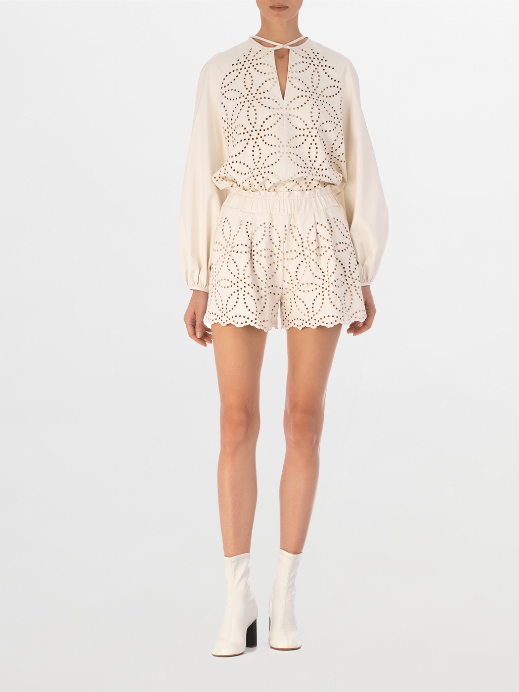 The Molveno Blouse Pearl is a white long-sleeve ecoleather blouse, featuring a geometric pattern on the front, a keyhole neckline, and a rounded hem.