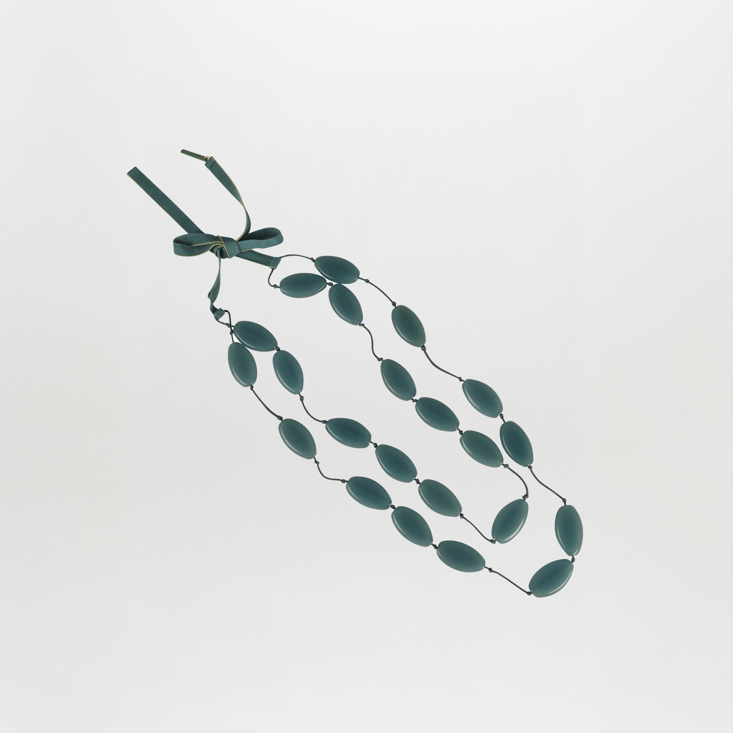 The Olivia Necklace Emerald is a triple-strand statement piece featuring oval-shaped teal Italian resin beads, linked and fastened with a matching teal ribbon bow, shown against a plain white background.