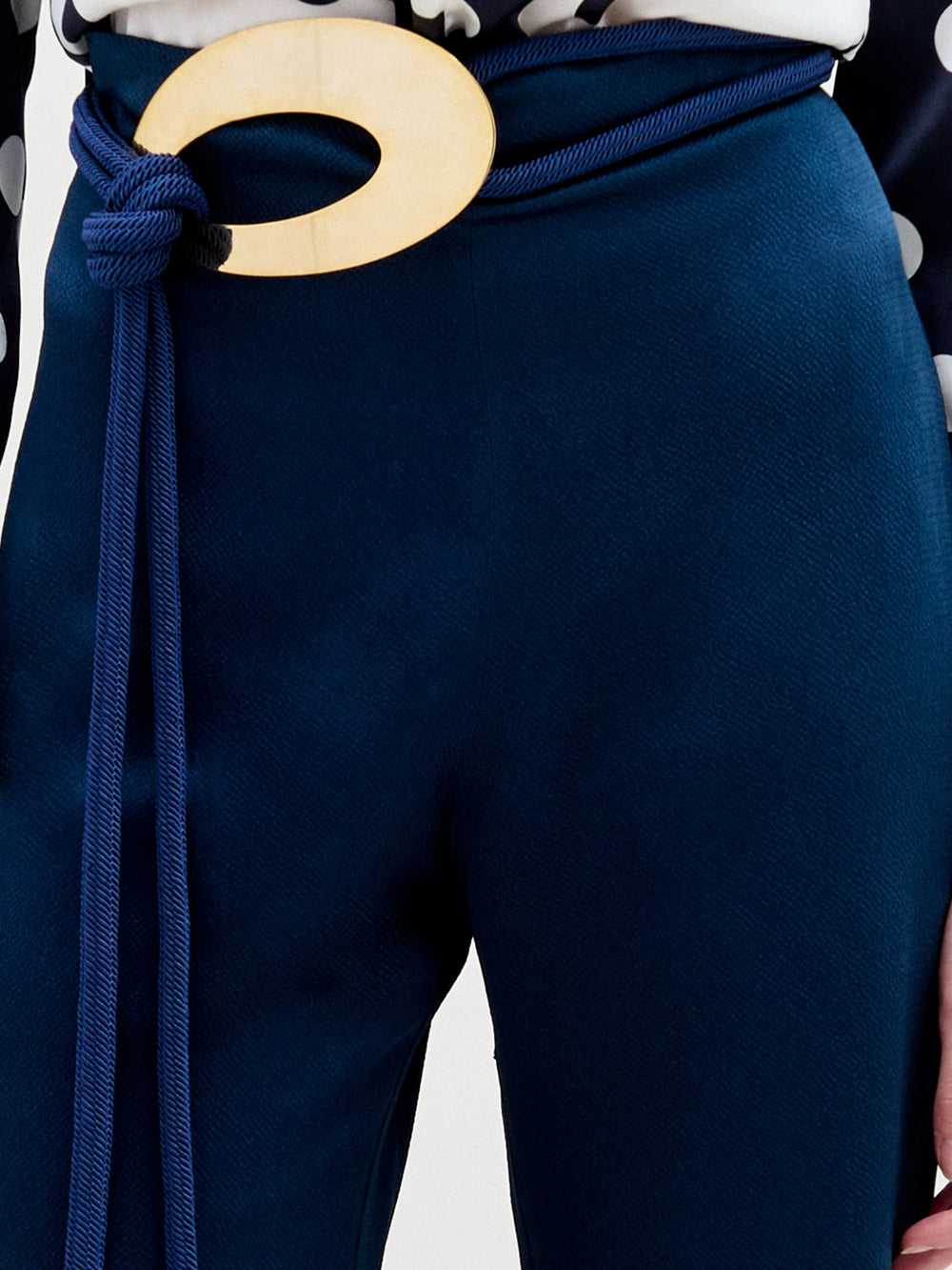 A person stands facing forward in a polka dot top with a keyhole cutout and high-waisted navy Palermo Pant featuring wide legs and a decorative gold belt, set against a plain white background.