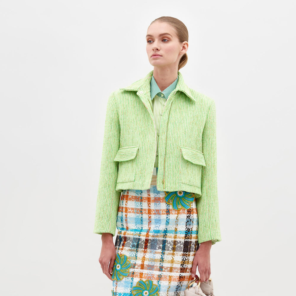 Person wearing the Perla Jacket Lime over a striped shirt and a colorful patterned skirt against a plain white background, showcasing a pre-order fashion piece for 2025.