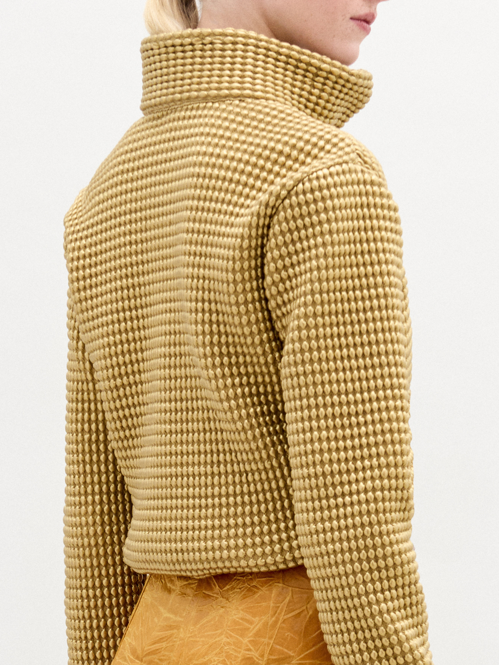 A woman wears the Zalta jacket, a brown sweater with an oversized fit, paired with gold pants.