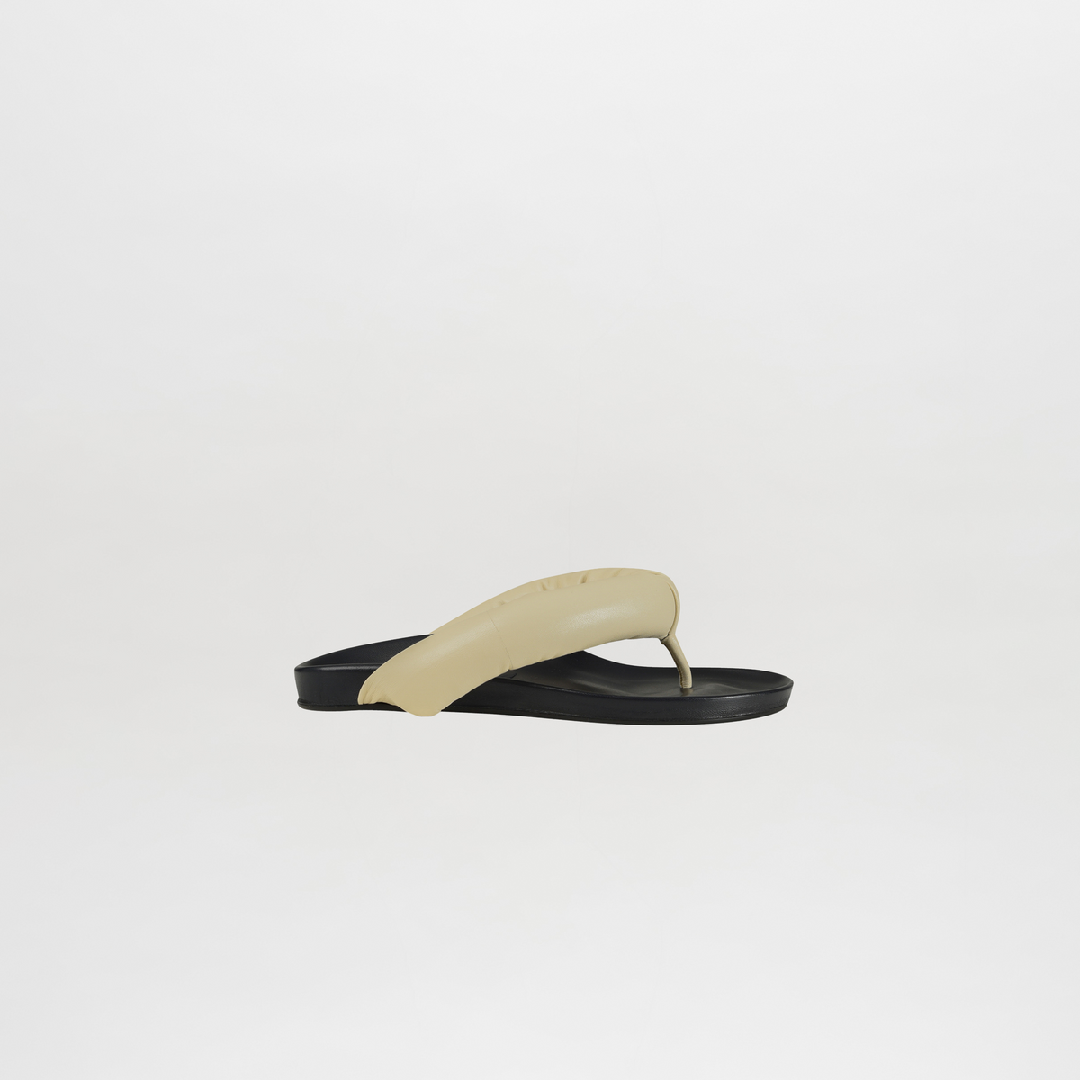 Flip-flop sandal with beige strap and black sole on a light gray background