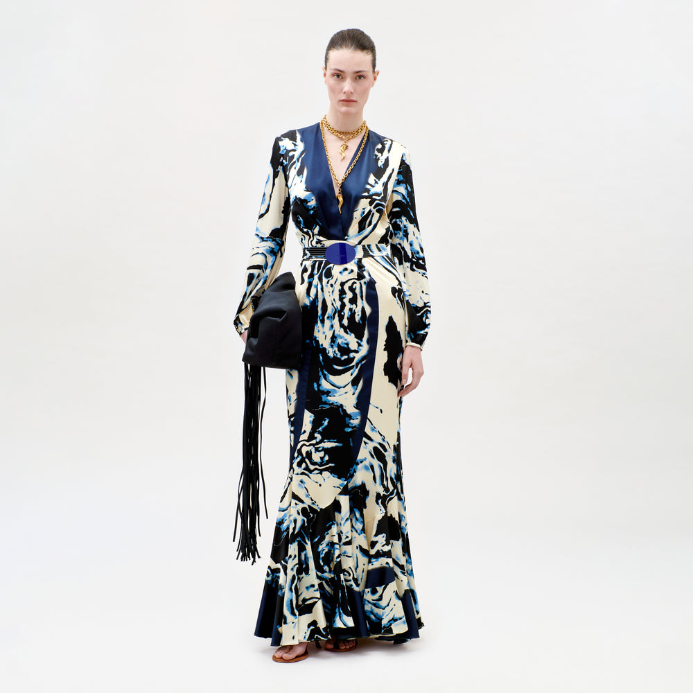 Model wearing a long, patterned dress with a black handbag on a white background