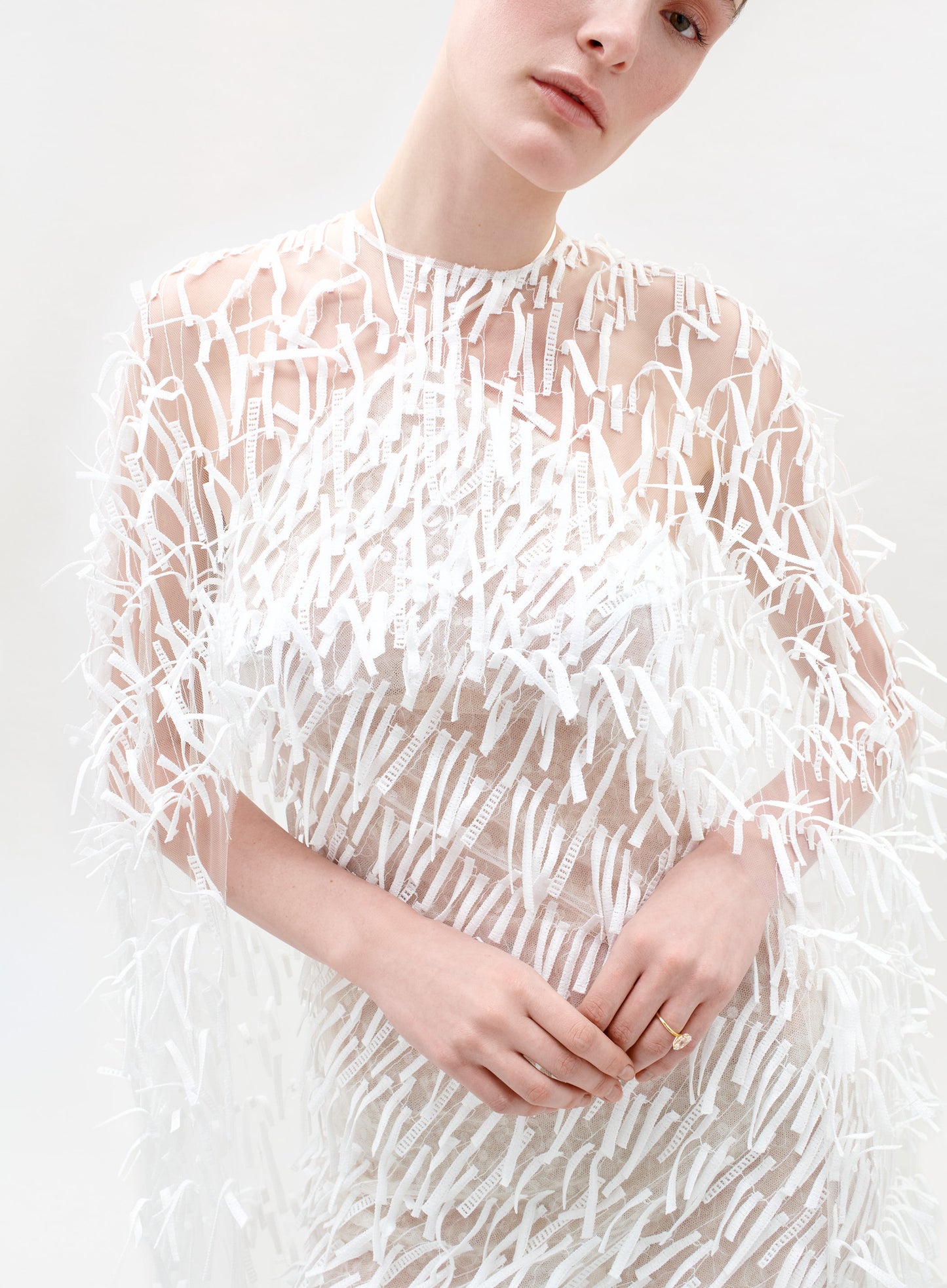 Person wearing a sheer white dress with a textured pattern on a white background