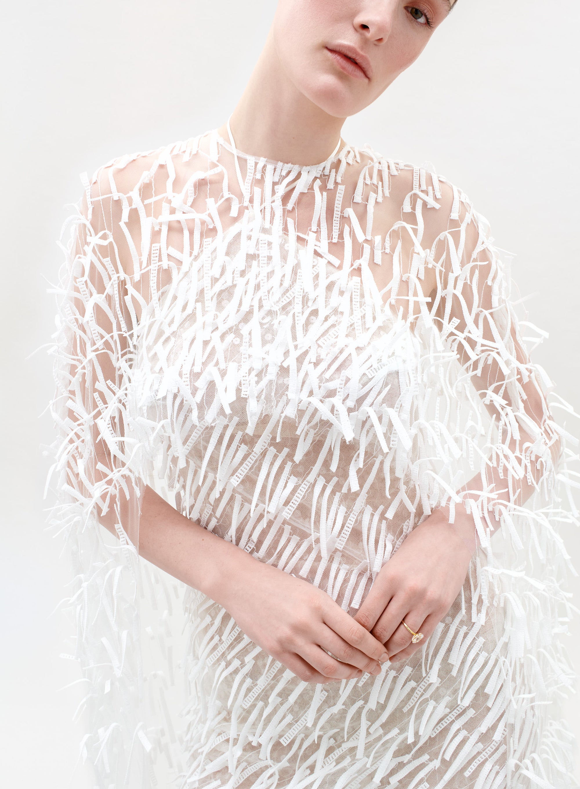 Person wearing a sheer white dress with a textured pattern on a white background