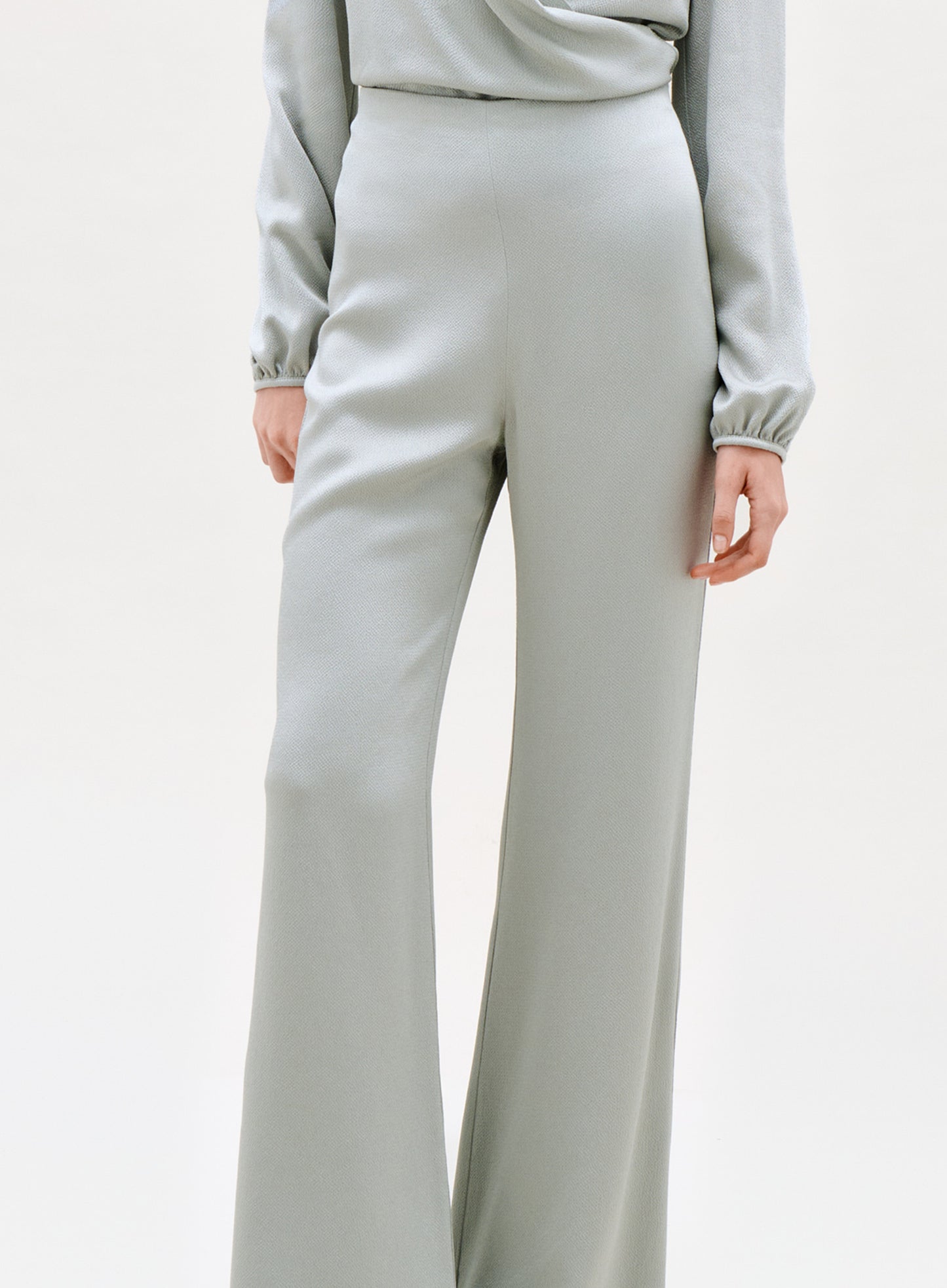 A person wearing the Palermo Pant—high-waisted, light gray wide-leg pants—shown from mid-torso to feet with one hand by their side against a plain background.