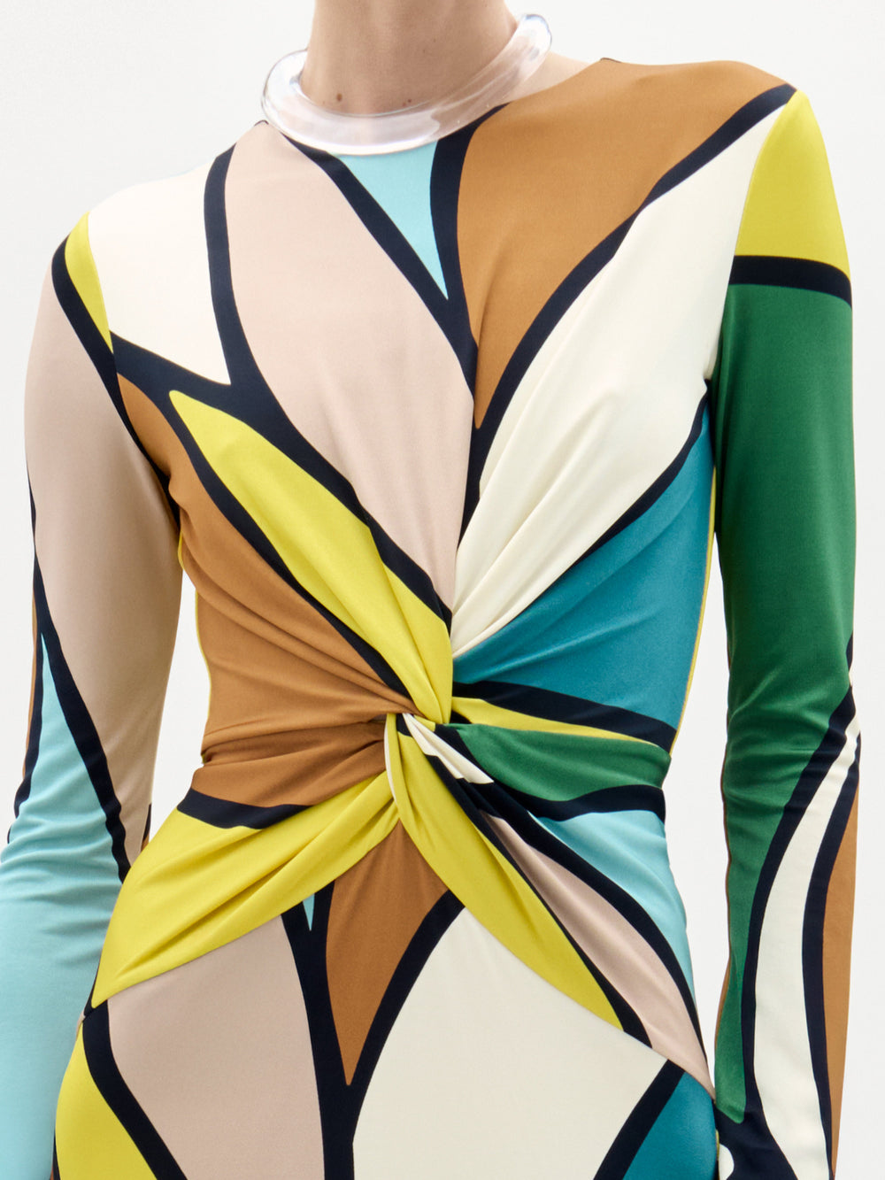 A woman models the Lucian Dress—a maxi with a form-fitting bodice, colorful abstract pattern, and front twist detail—against a plain white background.