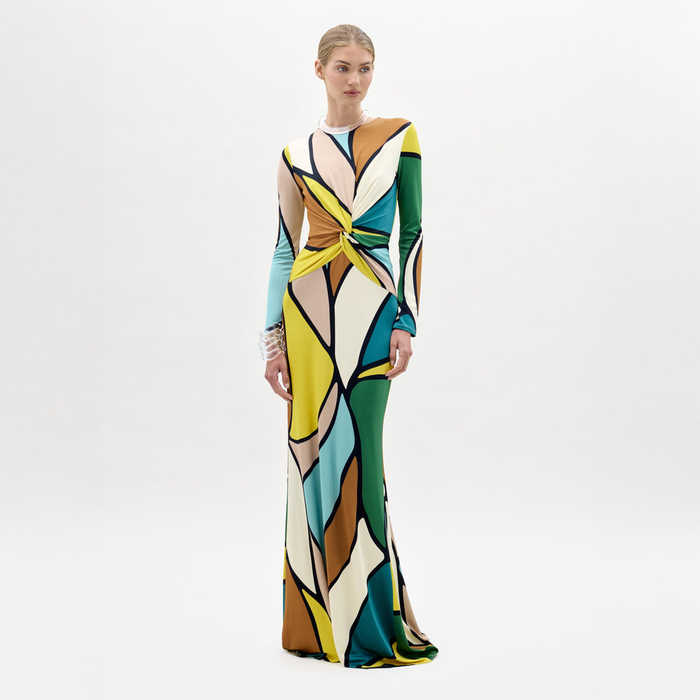 A woman models the Lucian Dress—a maxi with a form-fitting bodice, colorful abstract pattern, and front twist detail—against a plain white background.