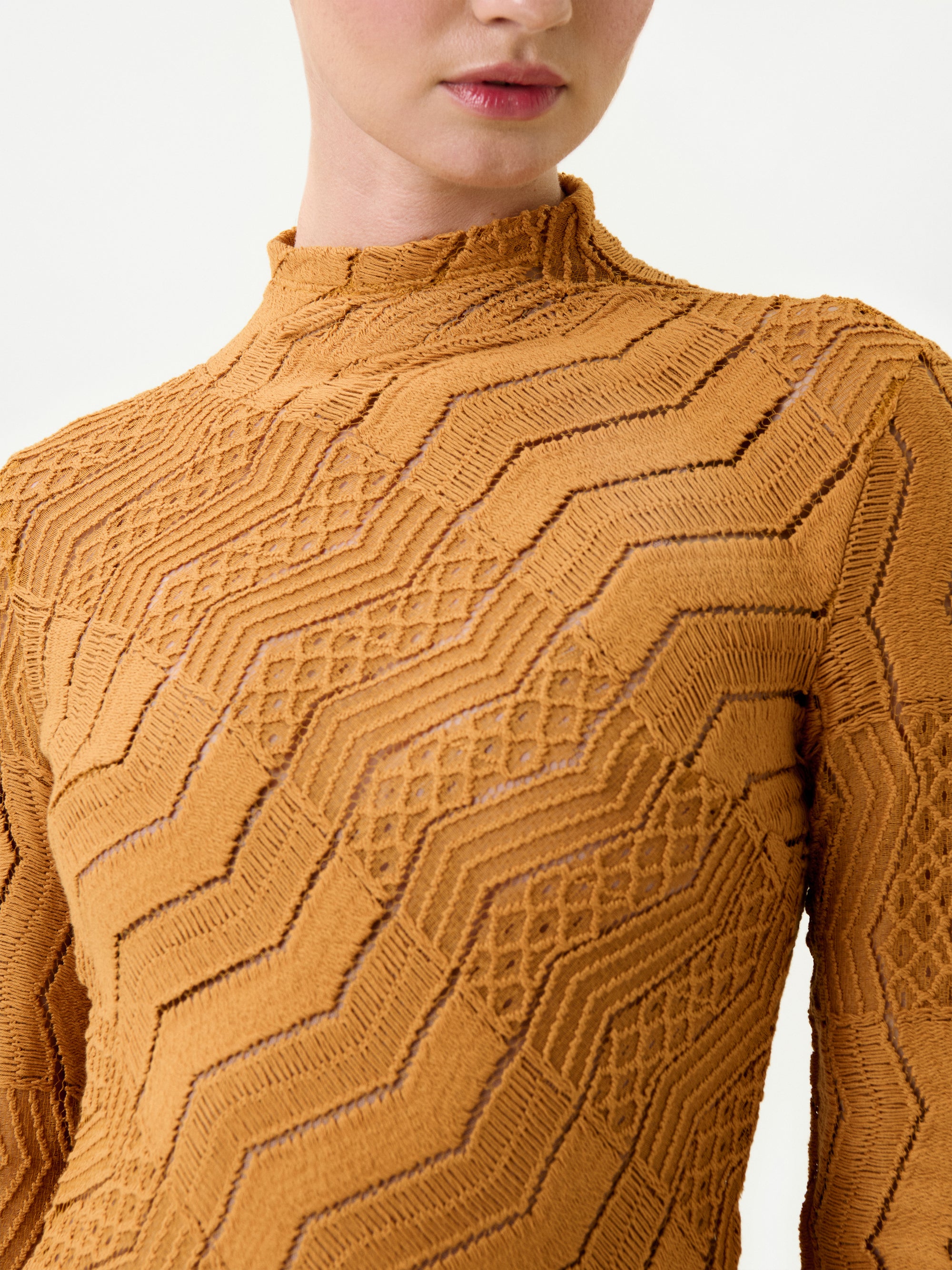 Close-up of a person wearing the Marianne Dress in mustard yellow, featuring geometric zigzag and diamond patterns on premium Italian fabric. The person’s face is partially visible against a plain white background.