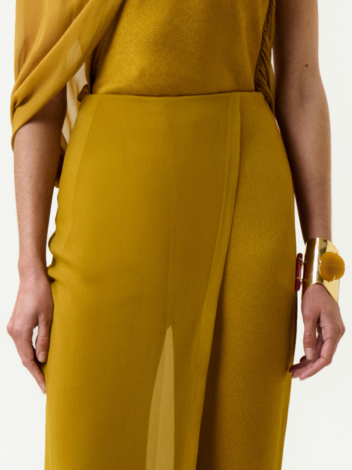 A person wears the Gaucin Pant in mustard yellow Italian fabric with draped silk, styled with a gold cuff bracelet, shown from shoulders to mid-thigh against a plain white background.