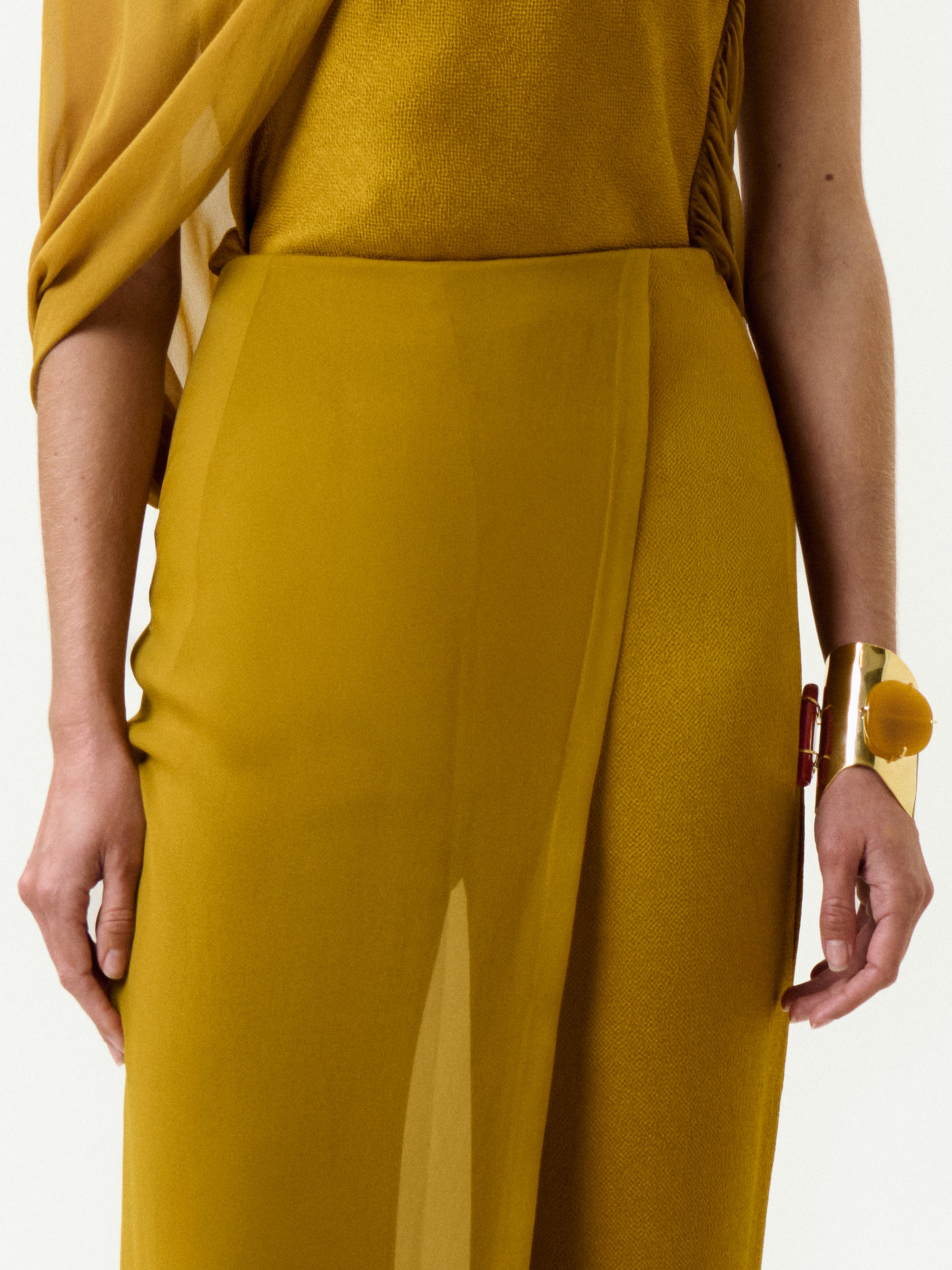 A person wears the Gaucin Pant in mustard yellow Italian fabric with draped silk, styled with a gold cuff bracelet, shown from shoulders to mid-thigh against a plain white background.