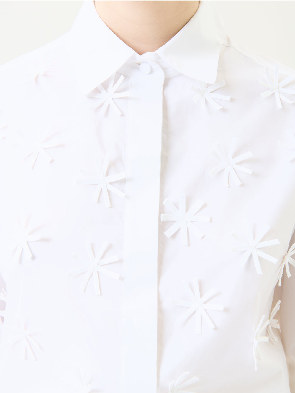 A person wears the Naroa Shirt, a white collared top featuring raised, asterisk-like patterns across the front. The photo is cropped to display only the upper chest, collar, and part of the neck.
