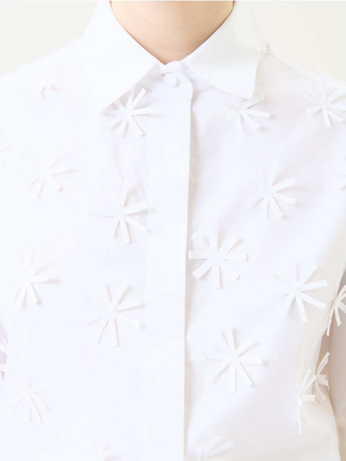 A person wears the Naroa Shirt, a white collared top featuring raised, asterisk-like patterns across the front. The photo is cropped to display only the upper chest, collar, and part of the neck.