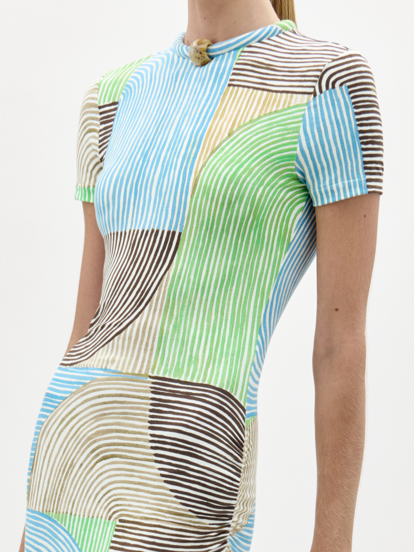 A woman in a Yara Dress, featuring multicolored patterns, stands holding a large beige fringe bag with circular handles against a plain white background.