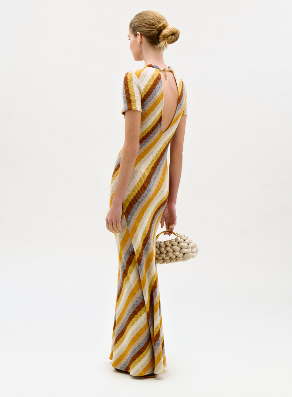 Woman wearing a striped dress holding a woven bag on a white background
