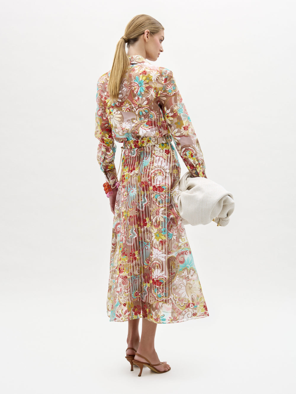 Woman wearing a floral dress holding a white handbag on a white background