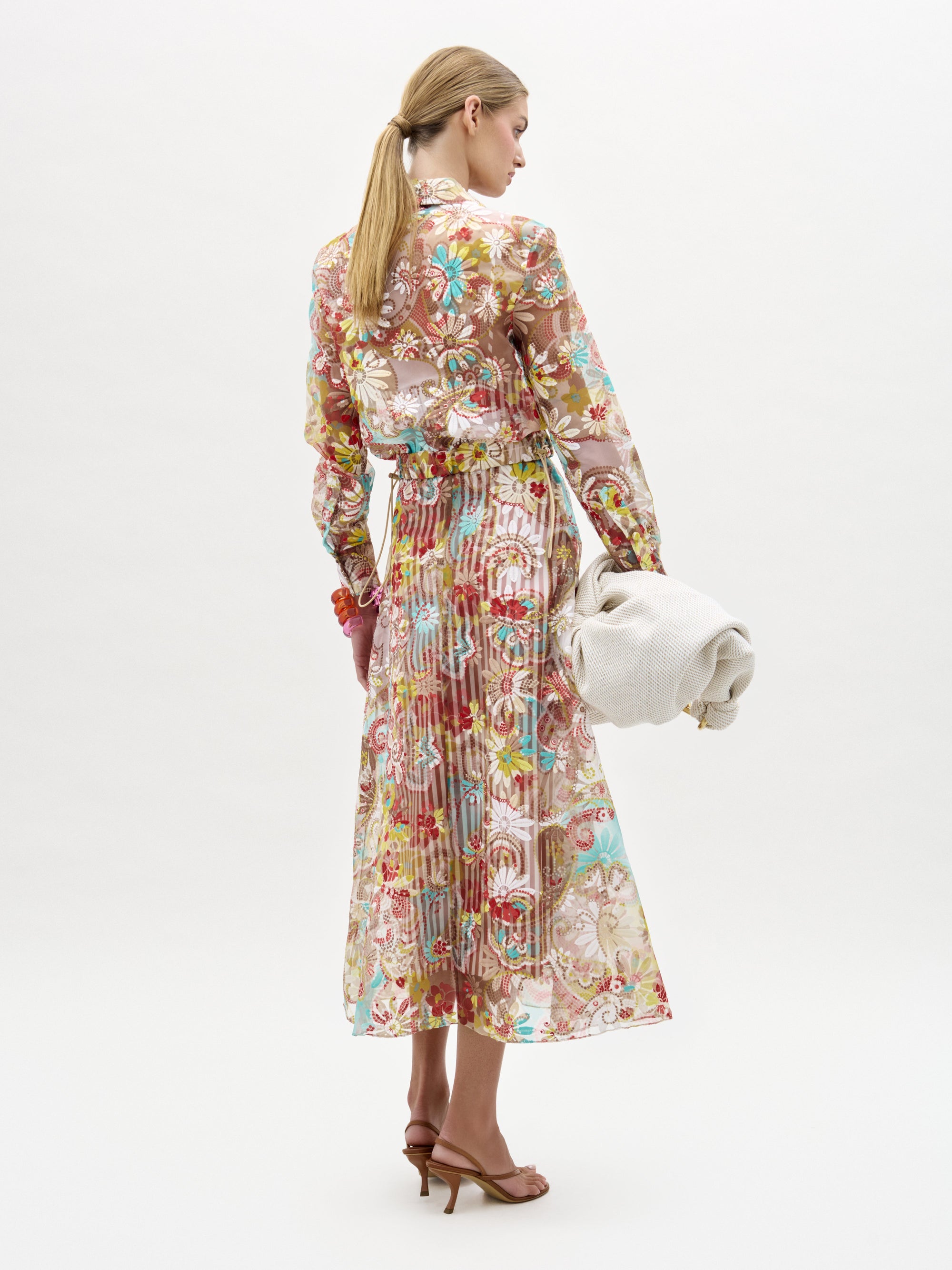 Woman wearing a floral dress holding a white handbag on a white background