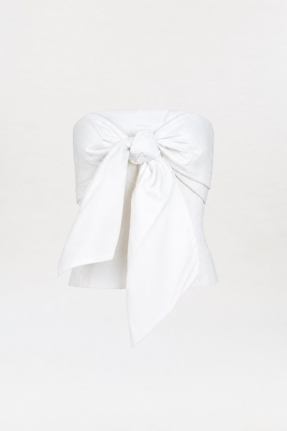 The Kacy Top is a strapless white top featuring a large, prominent bow tied at the bust, displayed on a plain white background.