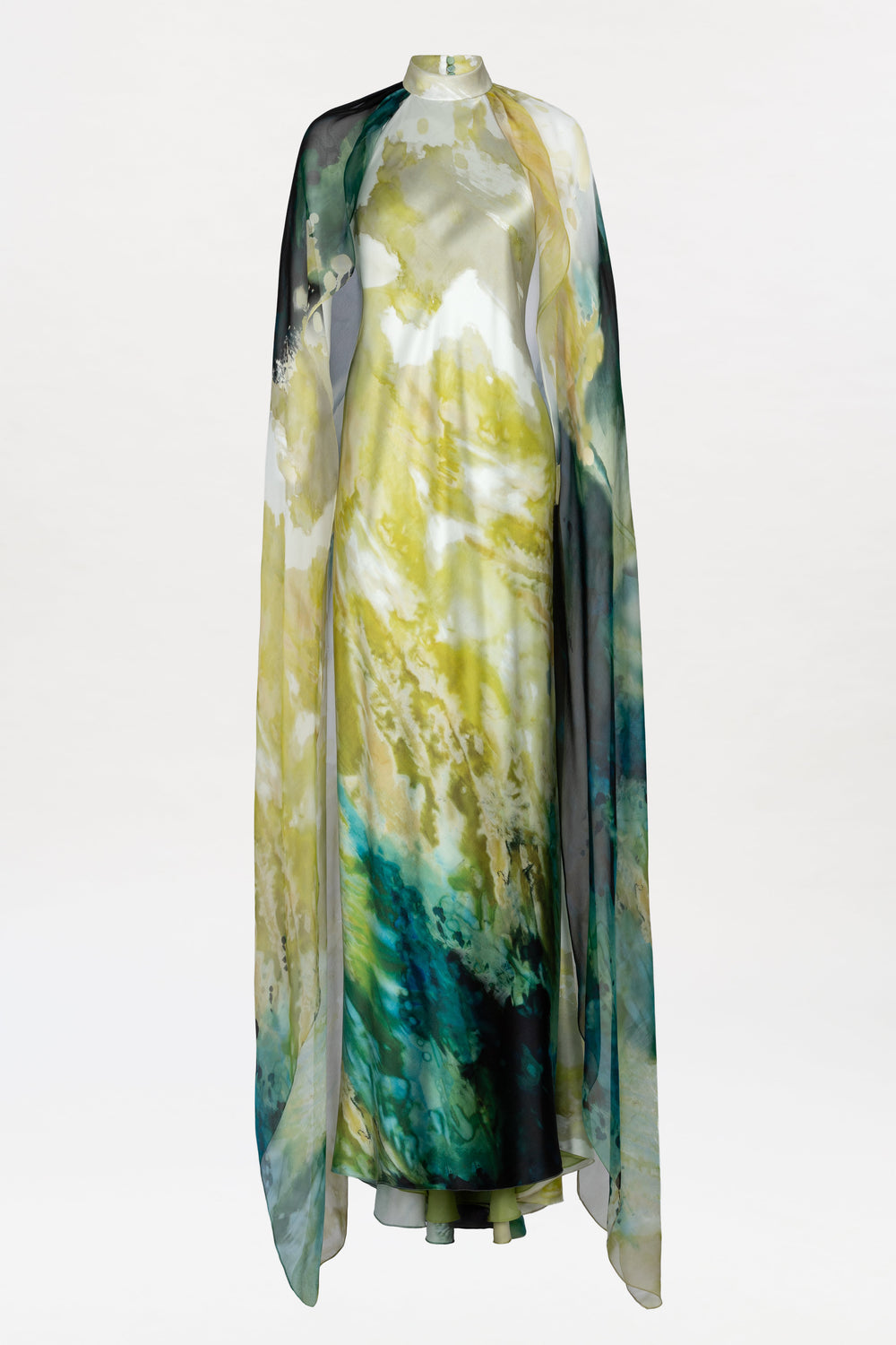Discover the Sabina Dress: a flowing, floor-length gown adorned with a watercolor-inspired pattern in yellow, green, blue, and black. This elegant design is completed with a sheer, matching cape draped gracefully over the shoulders.