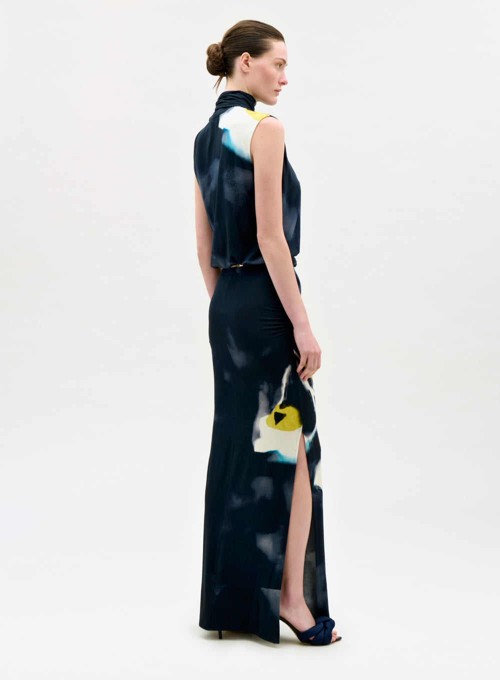 Woman wearing a long, dark-colored dress with abstract patterns on a white background
