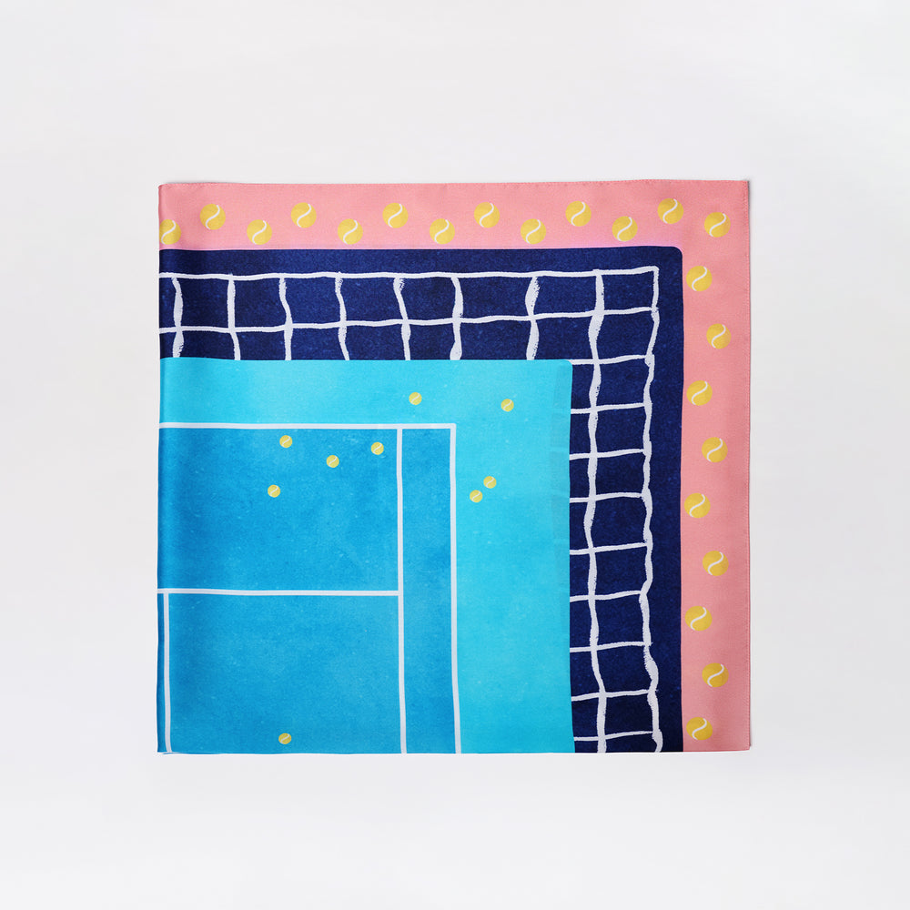 The Tennis Scarf is a square, colorful scarf with a blue tennis court design, navy grid pattern, and a pink border accented by yellow tennis balls. Background is plain white.