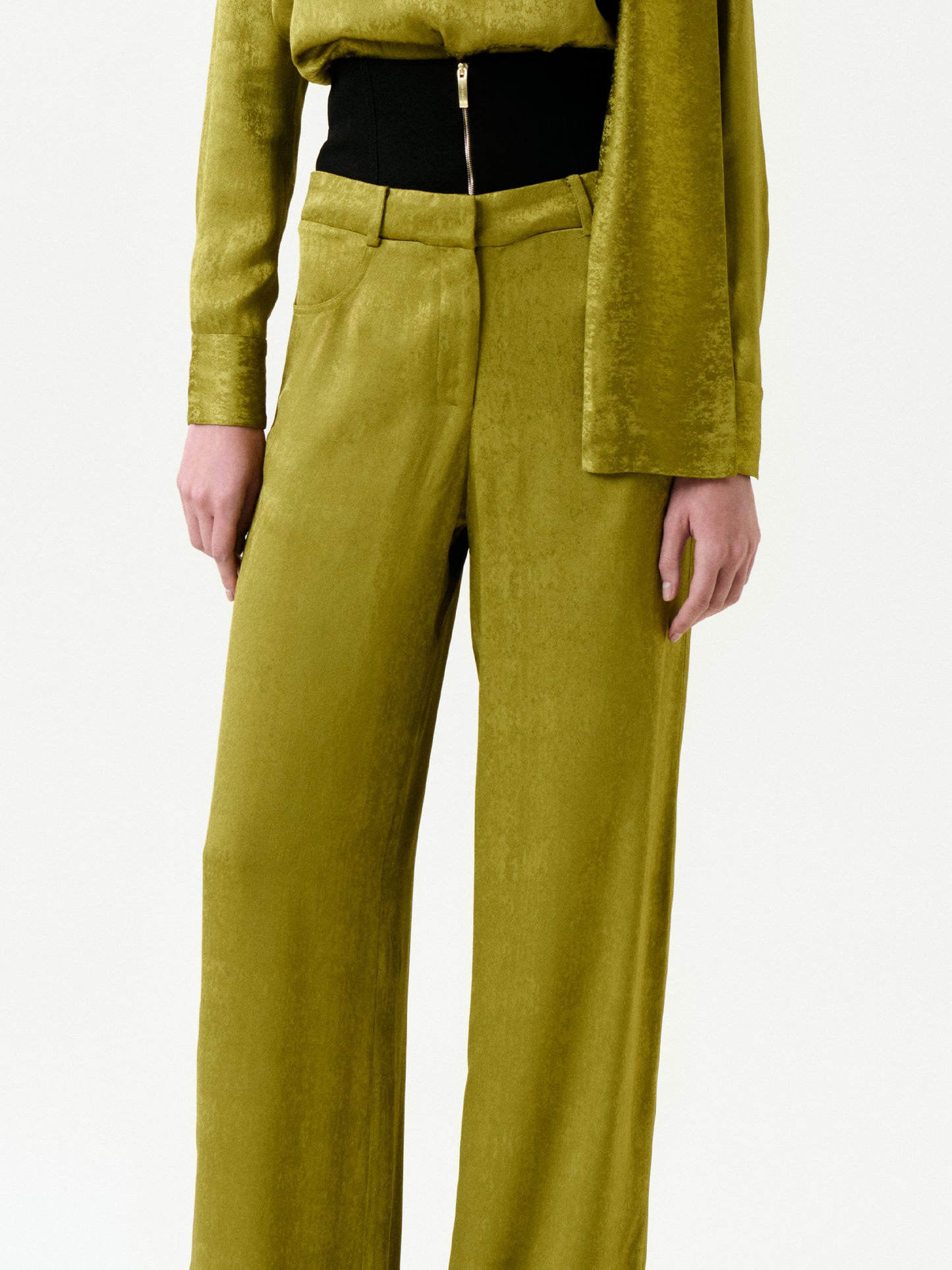 A person wearing the Karel Pant in textured olive green with a matching long-sleeve top and black waist belt, crafted from Italian fabric, shown from shoulders to feet against a plain background.