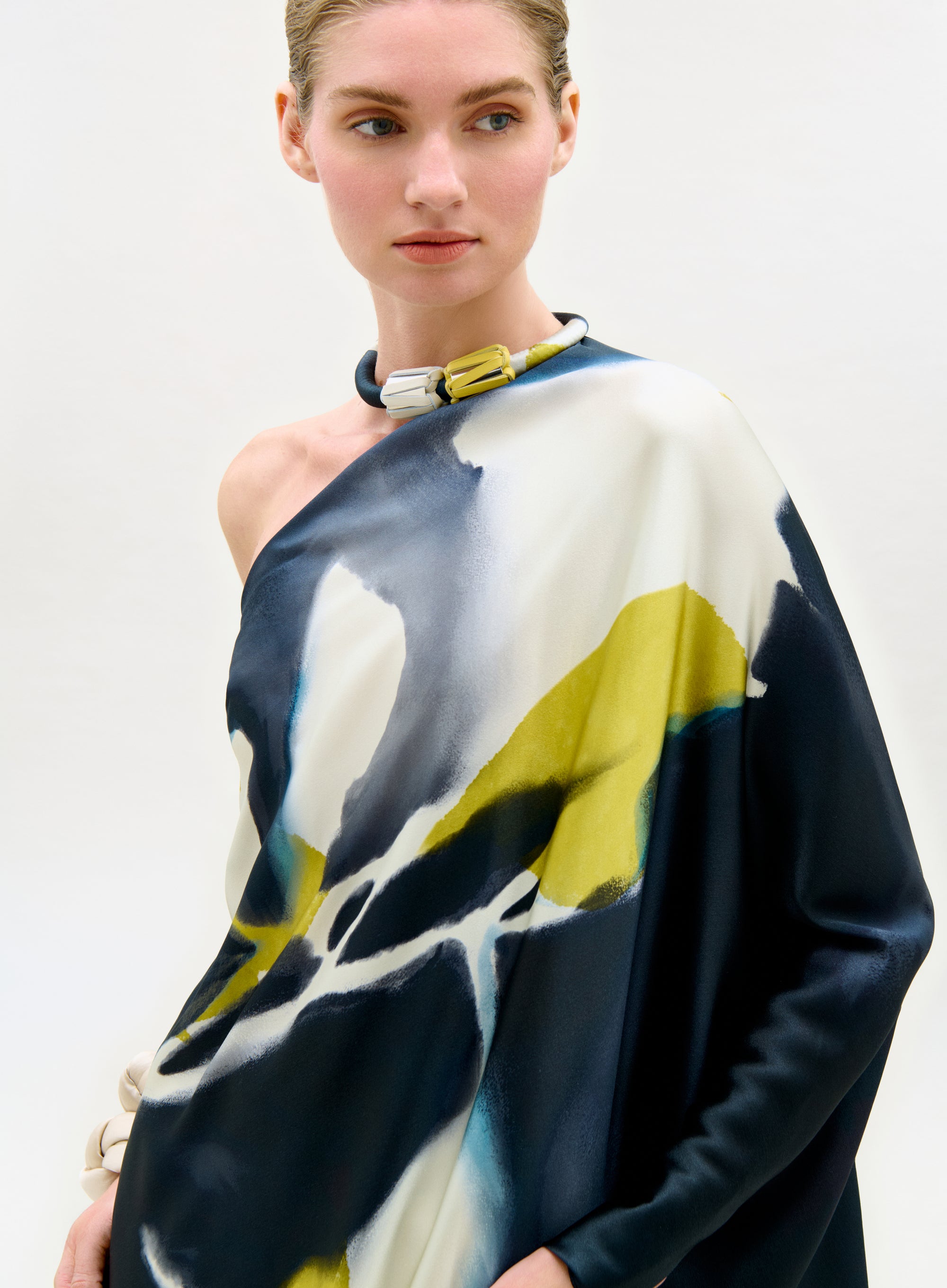 Model wearing a colorful one-shoulder top with abstract design on a plain background