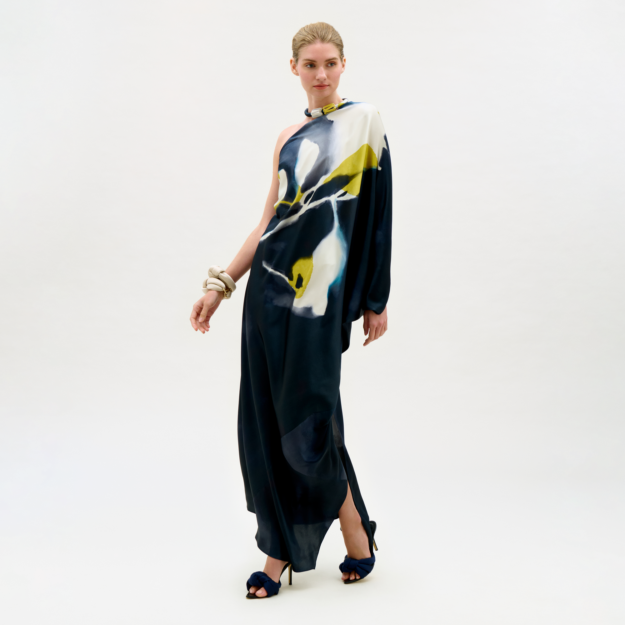 Woman wearing a long, dark blue dress with abstract white and yellow patterns on a white background