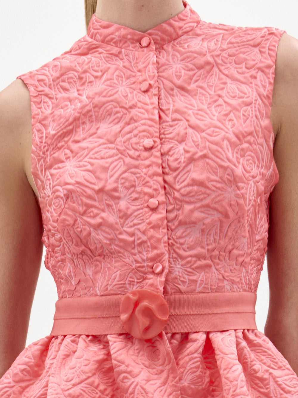Woman wearing the Colony Blouse, a sleeveless, textured pink top with a fitted bodice and peplum hem, standing against a plain white background.