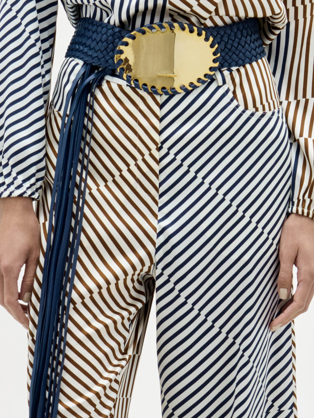 A woman stands against a plain background wearing the Emine Pant, styled with gold sandals and a matching choker.