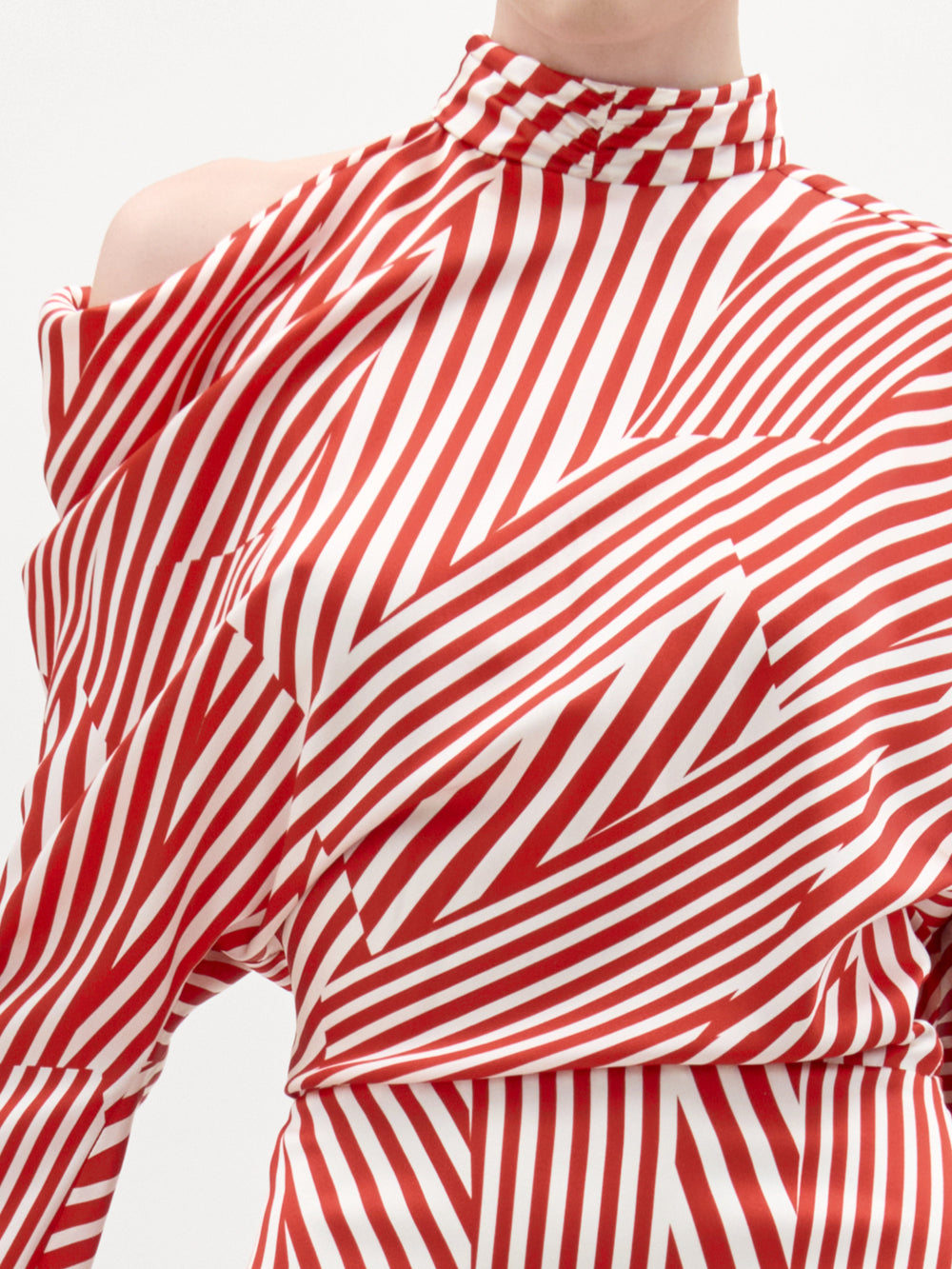 A woman stands against a plain background wearing the Lisa Dress—a red and white striped long-sleeve midi with an asymmetrical draped bodice—paired with a pink clutch and brown heeled sandals.