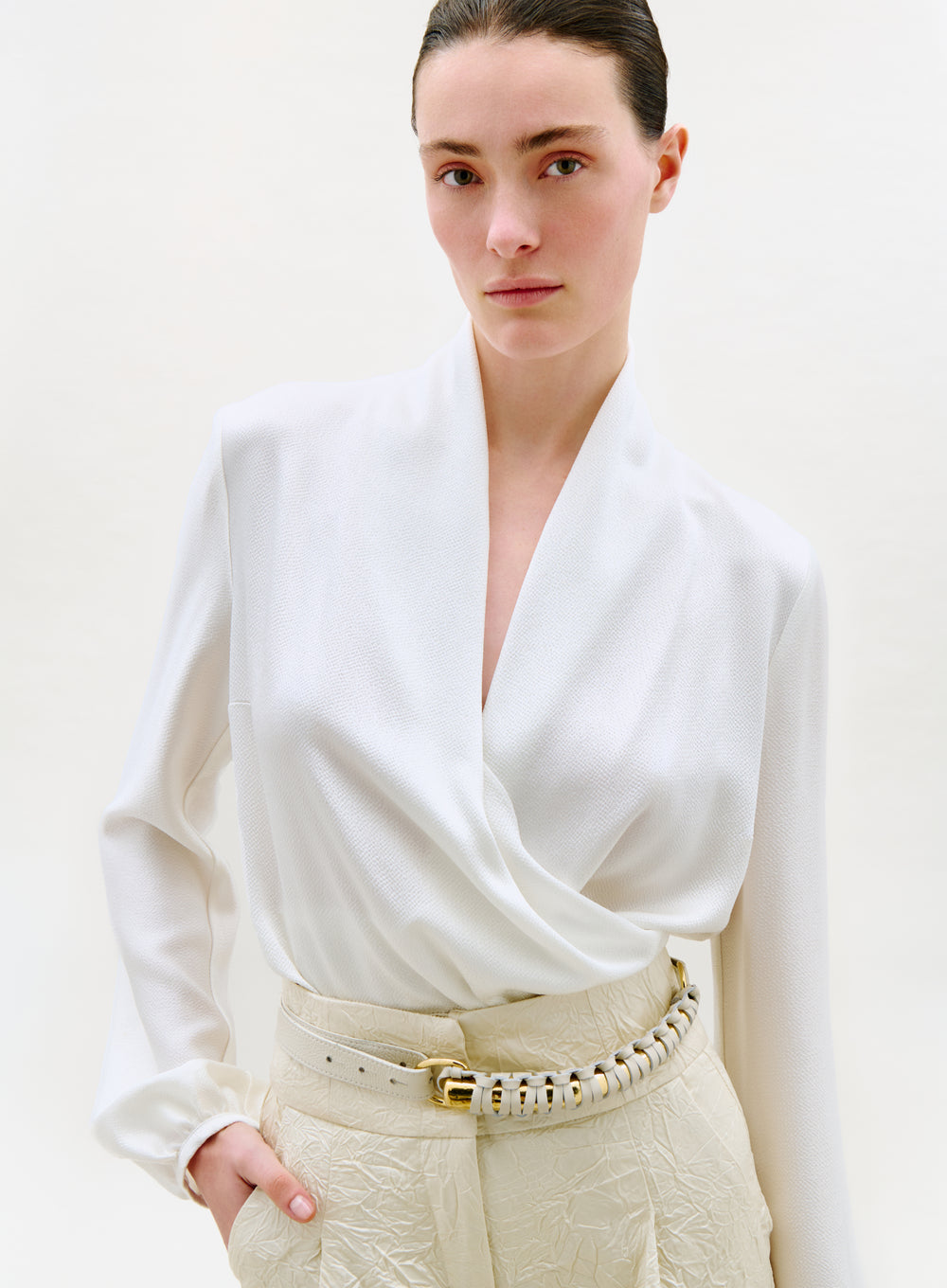 Woman wearing a white blouse and beige pants against a plain background
