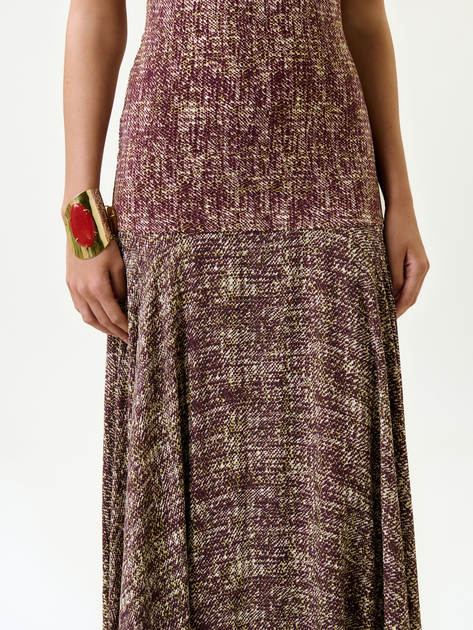A person wears the Leonore Dress, a dark red and yellow patterned maxi made from luxurious Italian fabric, paired with a large ornate gold cuff bracelet featuring a red stone.